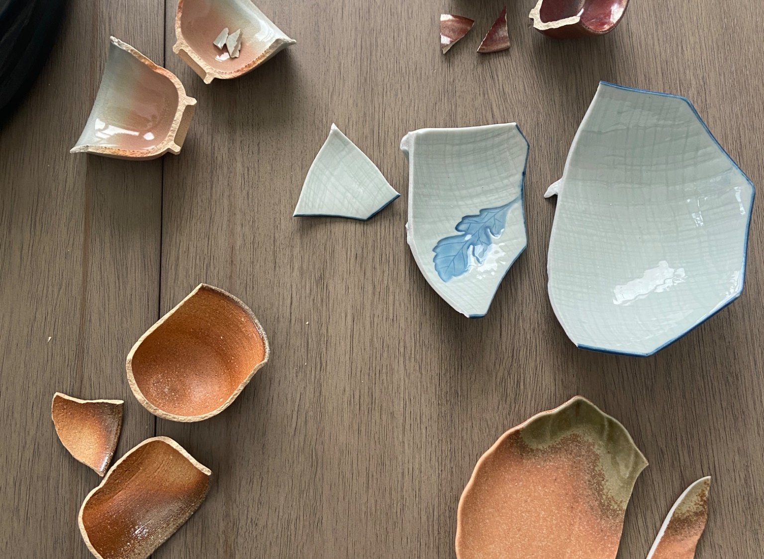Broken ceramic fragments laid out on a wooden table before repair