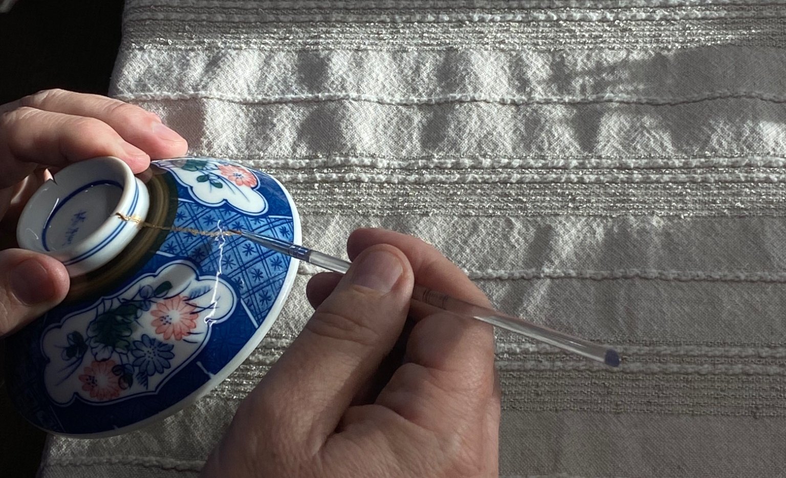 Close-up of gold being applied along the seam of a repaired porcelain bowl
